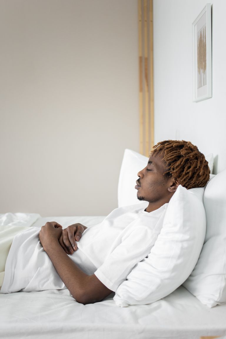 Peaceful scene of a man resting in a minimalist bedroom with white decor and natural lighting.